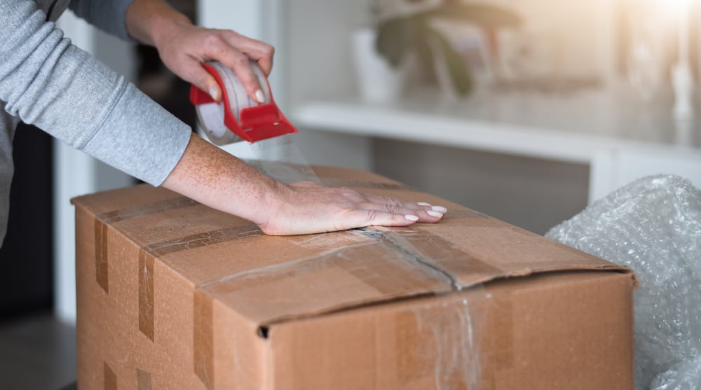 Close-up of hands taping a box shut carefully, TrekMovers